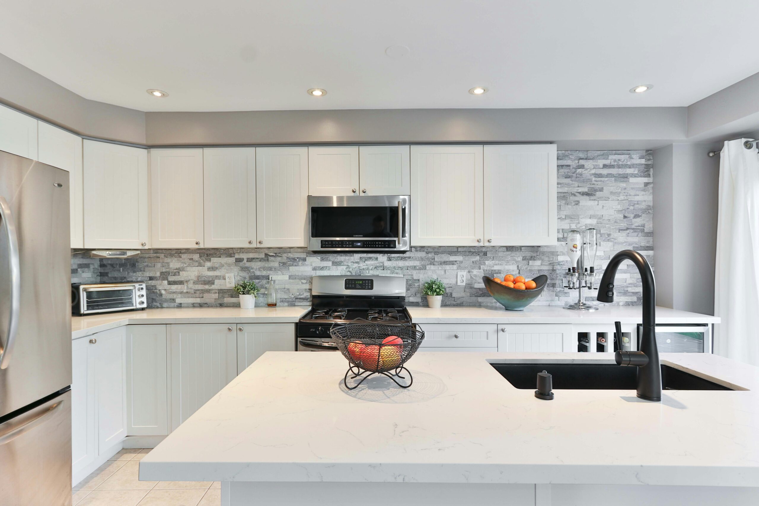 Sleek and modern smart kitchen with integrated high-tech appliances and white cabinetry, featuring a central island with a black countertop and advanced sink faucet, illuminated by natural light.